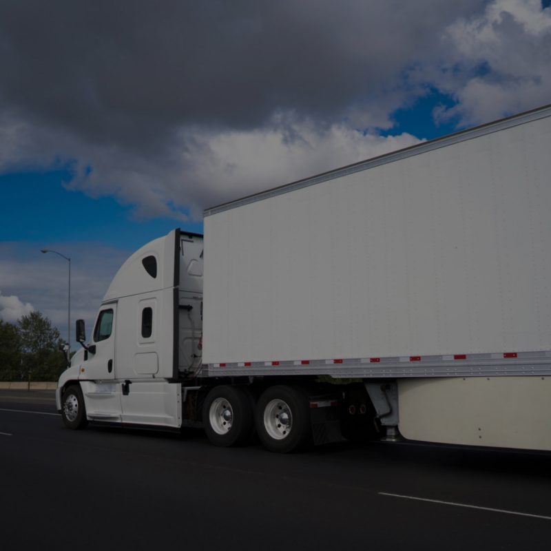 Stylish powerful long haul big rig white semi truck with high comfort cabin transporting commercial cargo in dry van semi trailer on the wide highway with cloudy sky